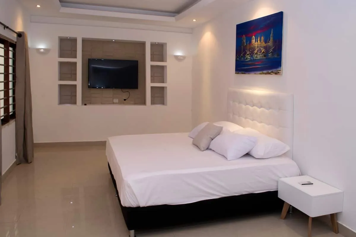Habitacion con cama blanca, televisor de pared y cielo raso decorativo