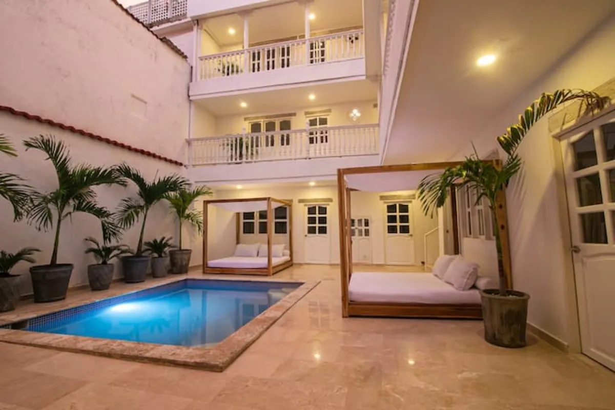 Piscina de patio iluminada en azul con palmeras y balcones superiores