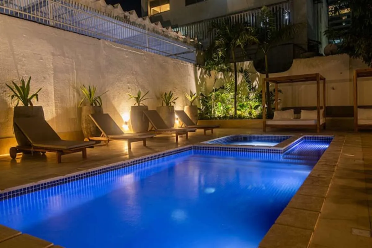 Blue-lit pool with loungers and garden wall at night